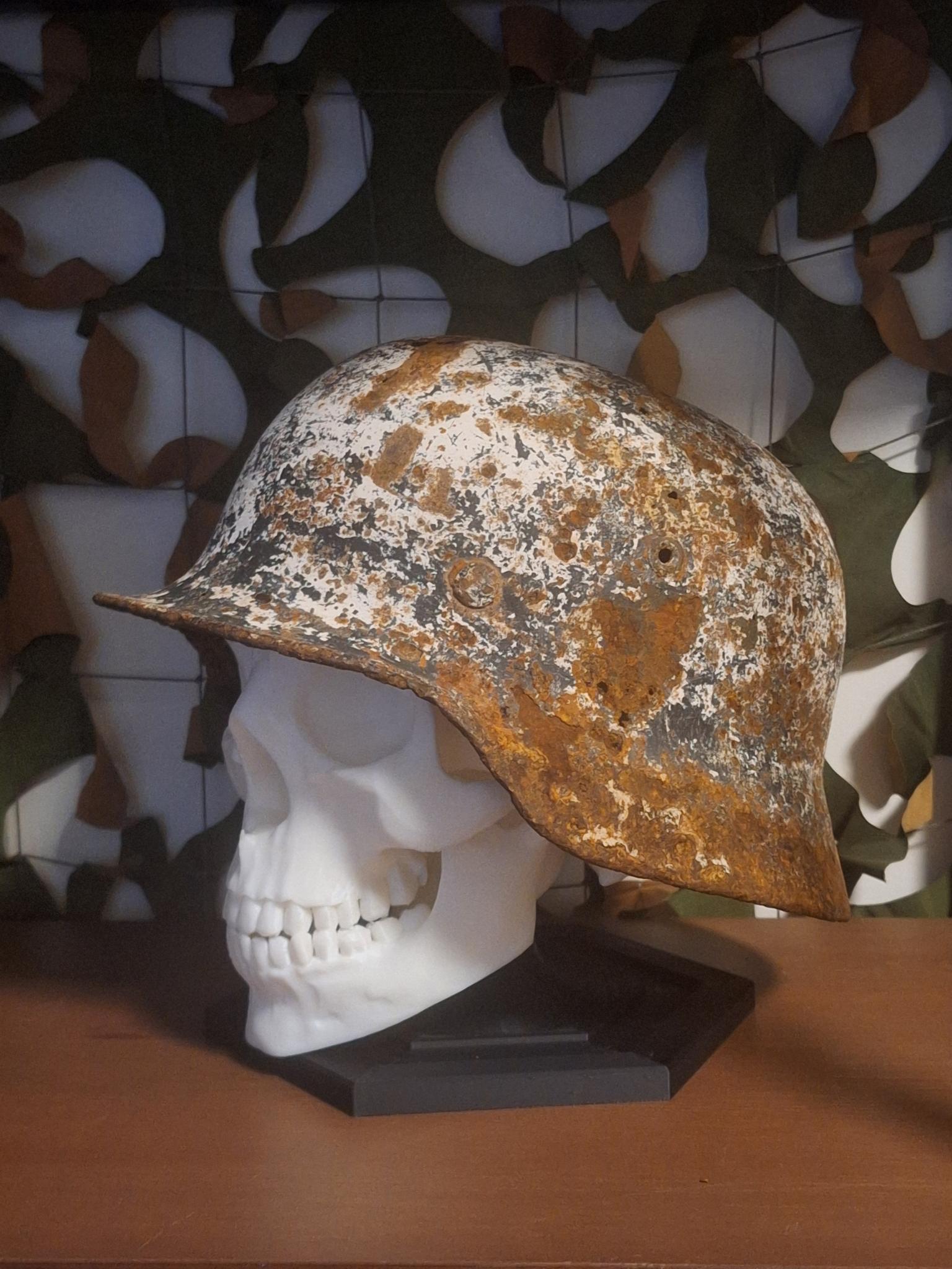 Rust-covered military helmet on a skull with camouflage-patterned background