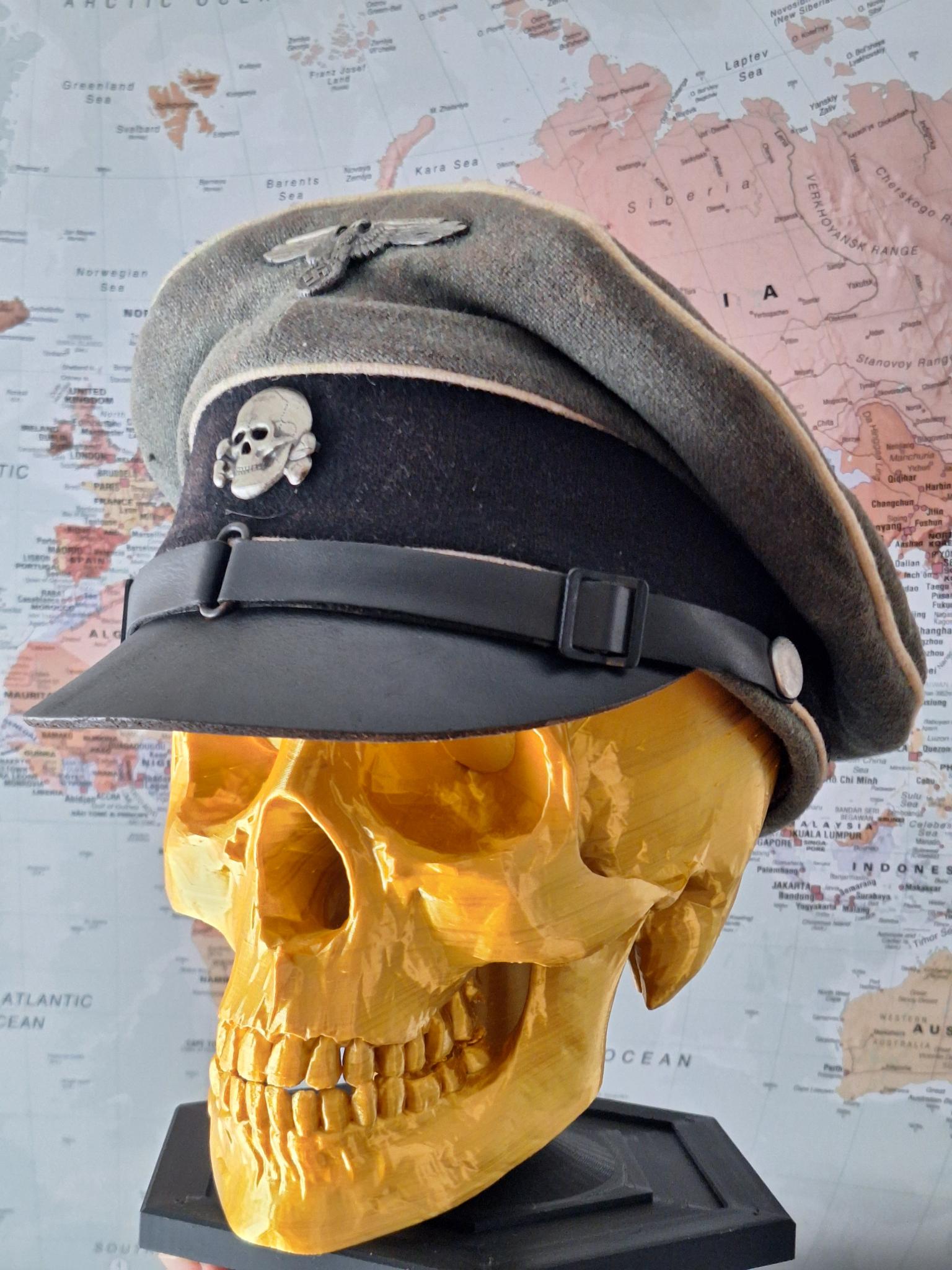 Gold skull with a military-style cap featuring skull and crossbones design on a world map background.